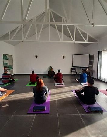a group of people practicing yoga inside a room - Neer Ganga Resorts