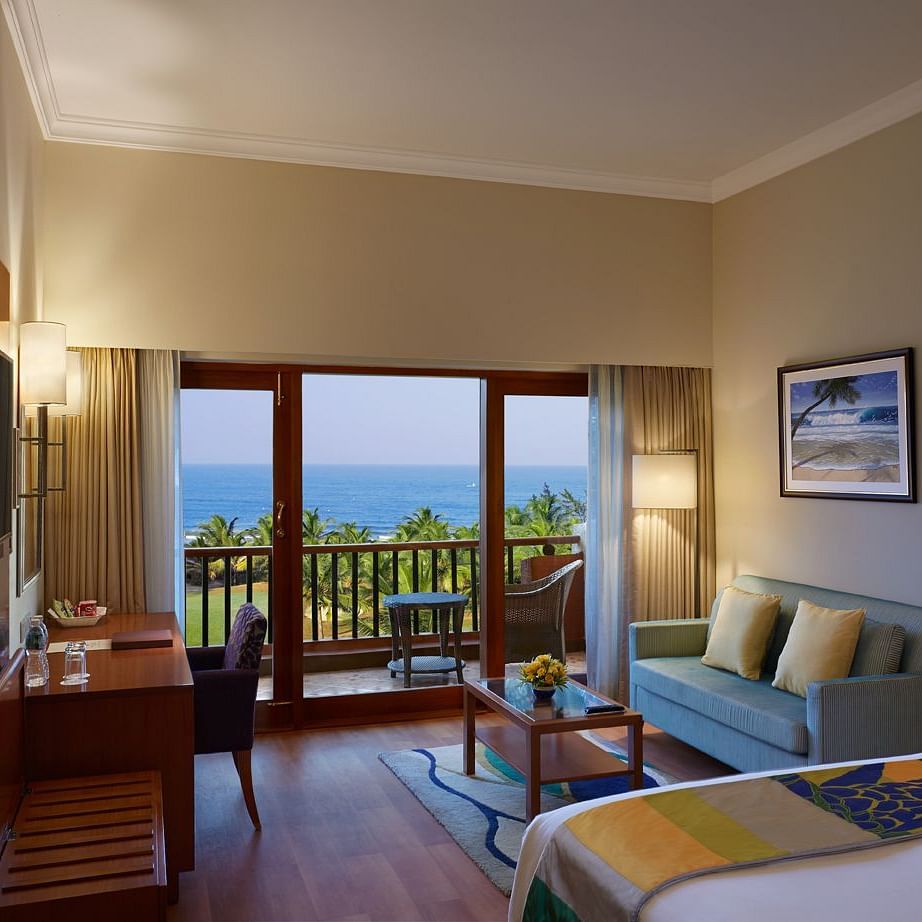 a double bed with a sofa, table, lamps and tv in view inside Ocean front view - Caravela Beach Resort Goa