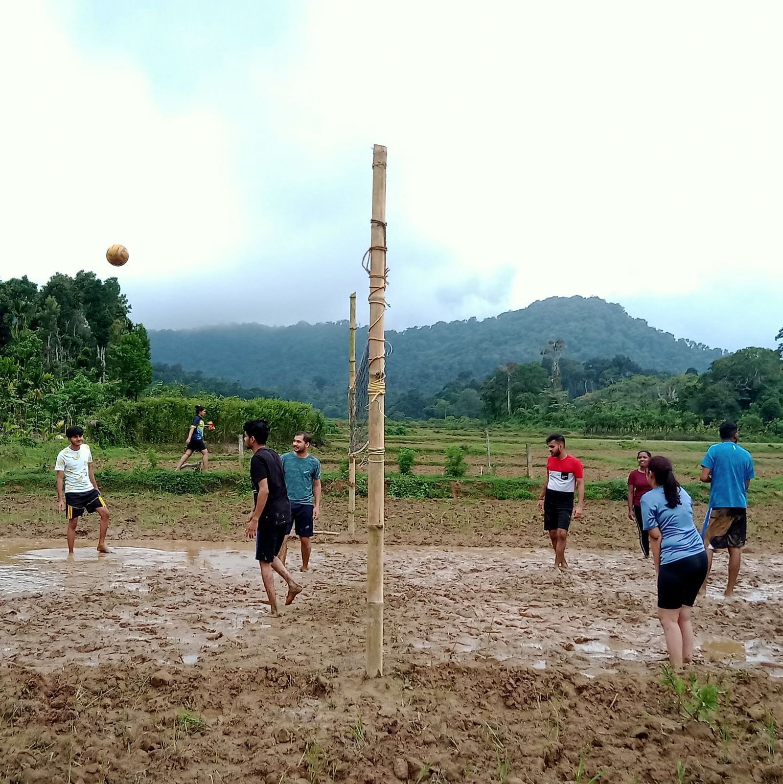 Group playing volleyball in a muddy field with a scenic mountain backdrop - Evergreen County