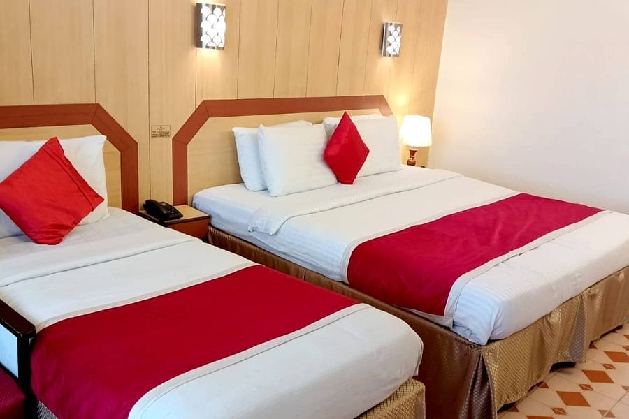 Room with a single bed, a double bed, bedside lamp, and wall-mounted lights at Hotel Swagath, Bangalore