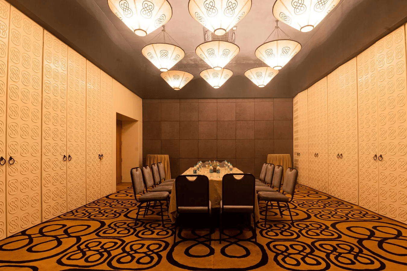A long conference table surrounded by executive chairs under hanging warm lights inside Dholavira banquet hall at 3102bce - A Vedic Resort by Lindsay.