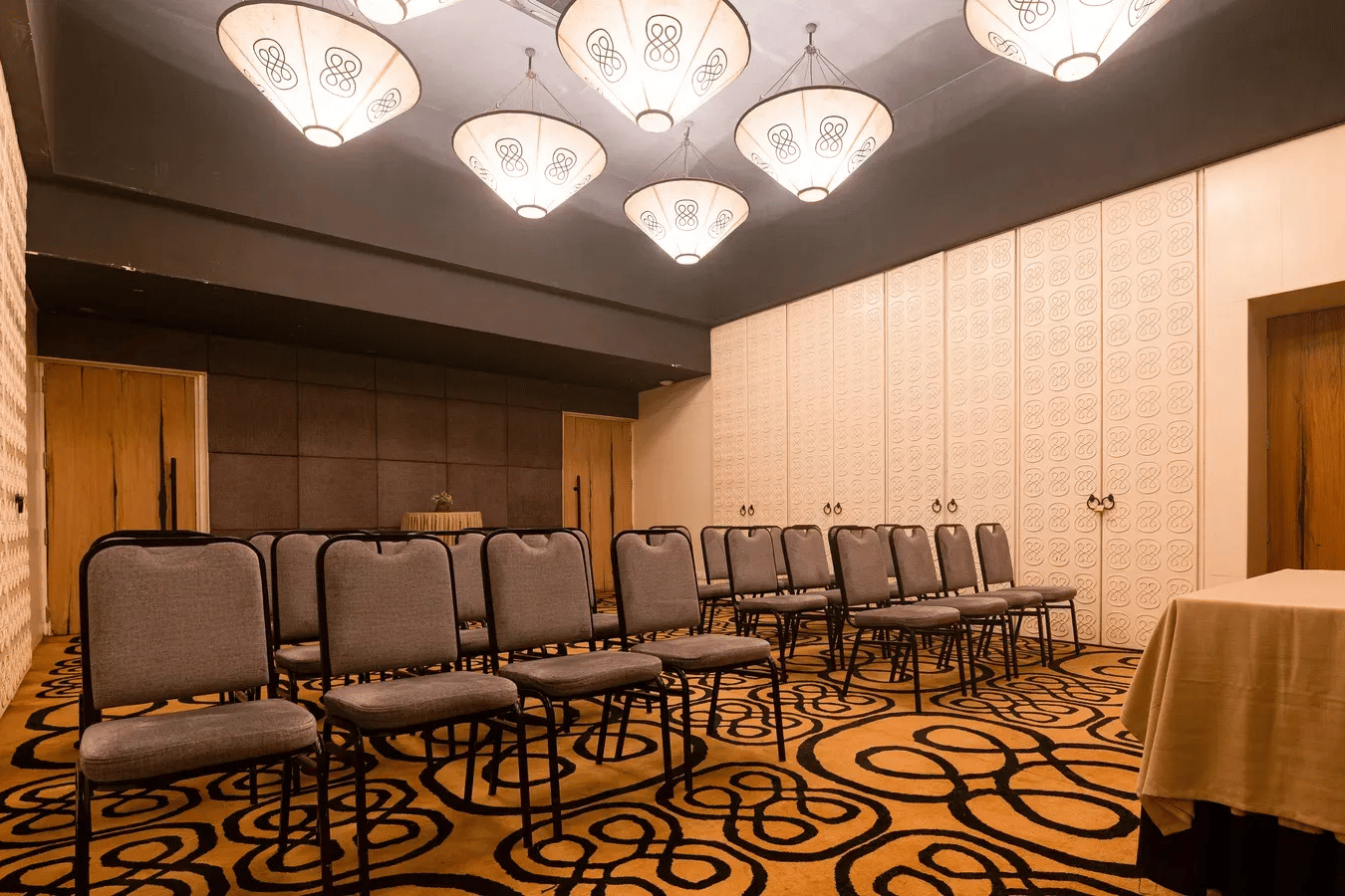Rows of grey upholstered chairs arranged in theatre style inside Dholavira banquet hall, illuminated by glowing ceiling lanterns at 3102bce - A Vedic Resort by Lindsay.