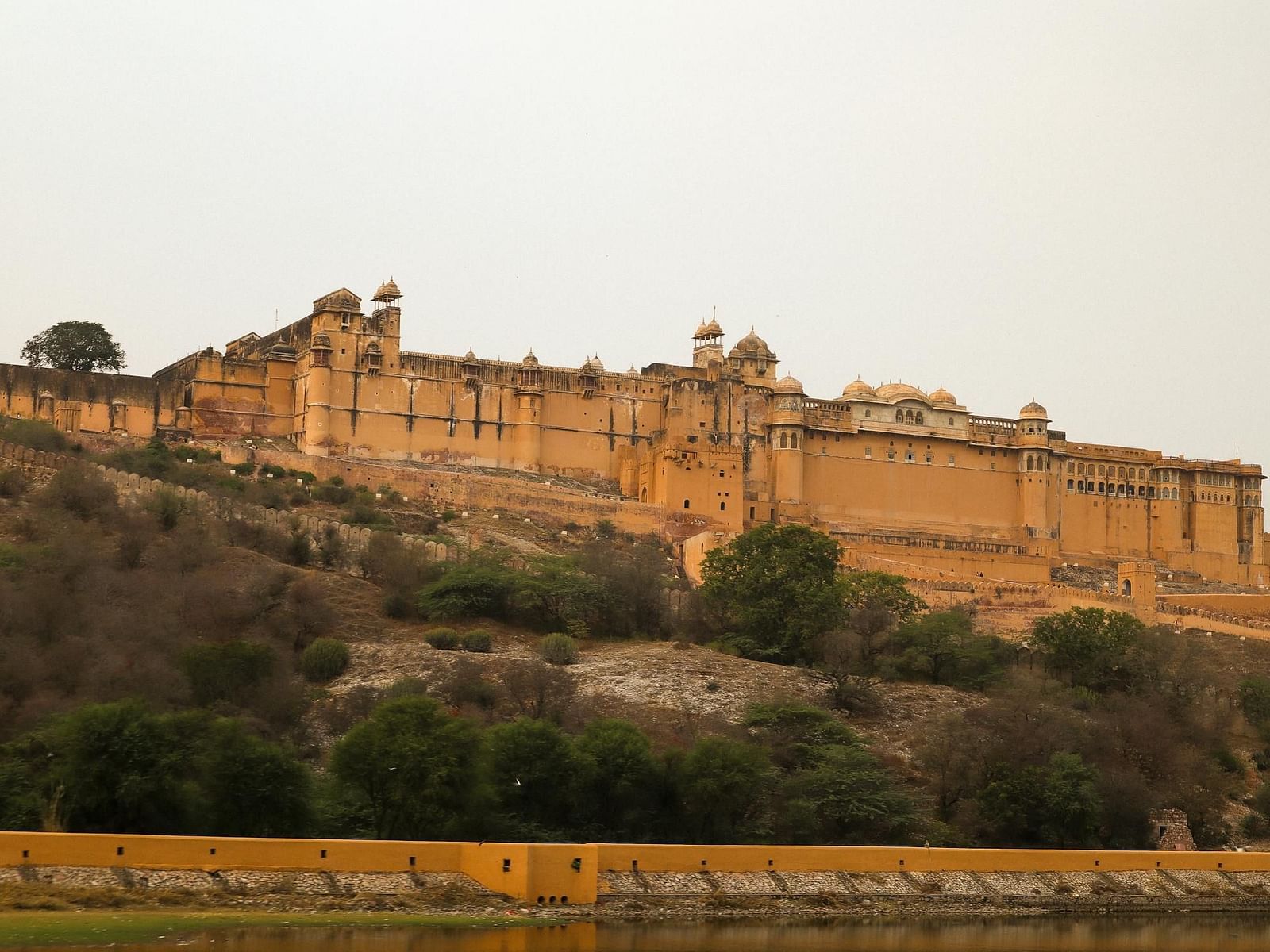 A sprawling fort complex with towers and walls extends across a hilly landscape under a hazy sky.