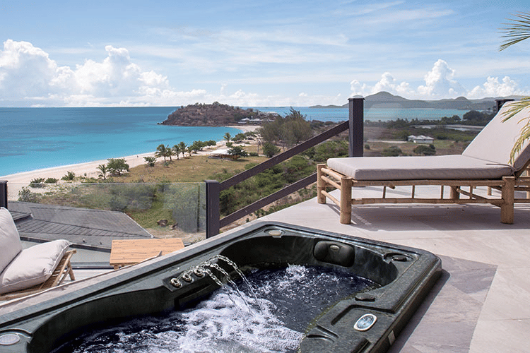 An outdoor terrace with a hot tub and lounge chairs, providing a stunning elevated view of the ocean and coastline.