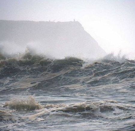 A stormy scene at Noyo Harbor with rough ocean waves crashing under a cloudy sky.