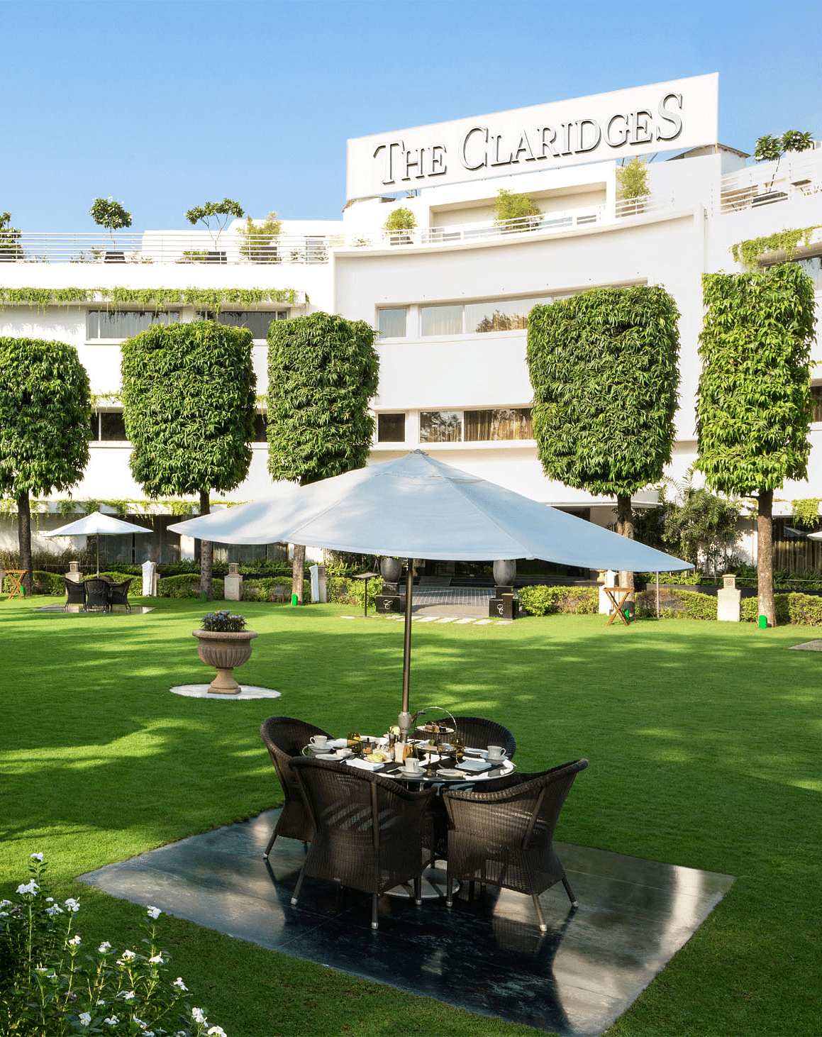 a beautiful landscape image of the claridges garden with glass top coffee tables scattered everywhere - The Claridges New Delhi