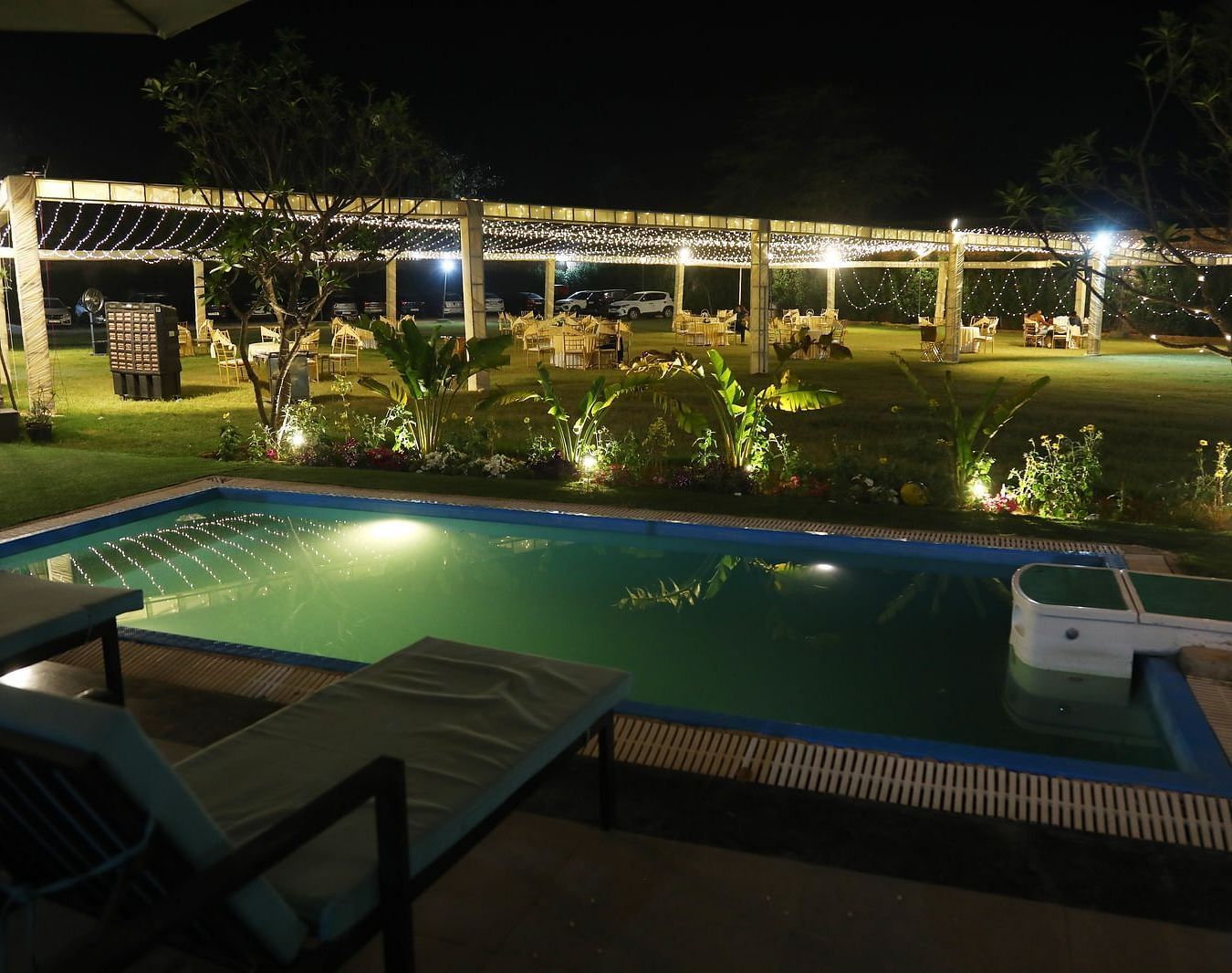 Swimming pool at Tisya Farms, Gurgaon with deck chairs and lighting, viewed during the night.