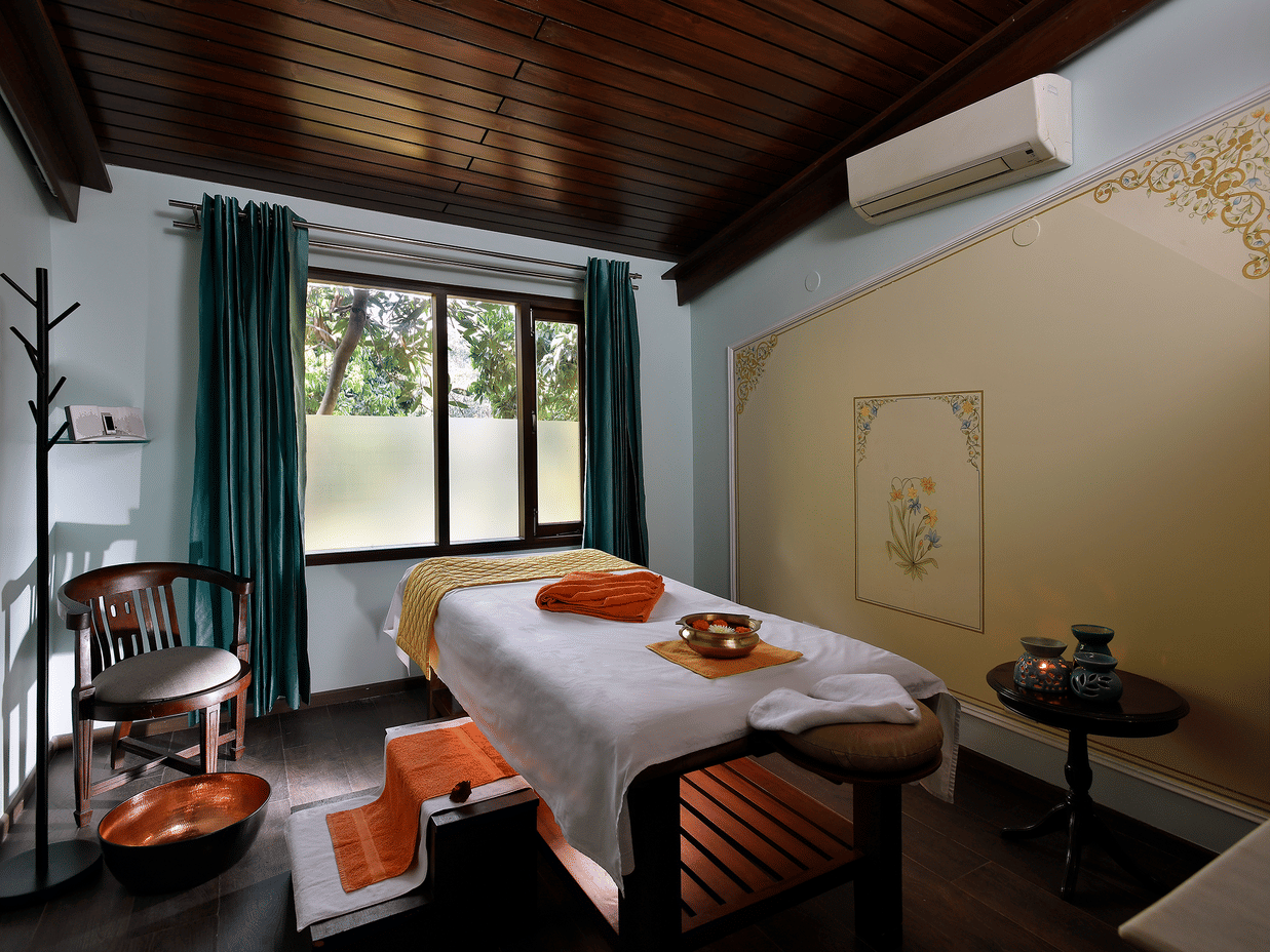A wide-angle shot of the spa room featuring a spa bed in the centre with ample of natural light coming inside from the window at Neemrana's Glasshouse on The Ganges, Rishikesh.