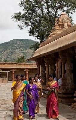 A stone temple structure with people walking along a colonnaded walkway.