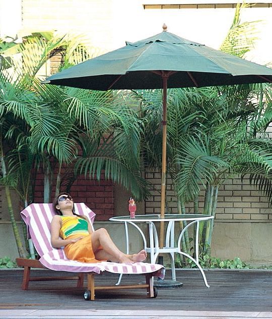 A woman laying on a lounging chair under an umbrella at Nirvana Luxury Hotel, Ludhiana.