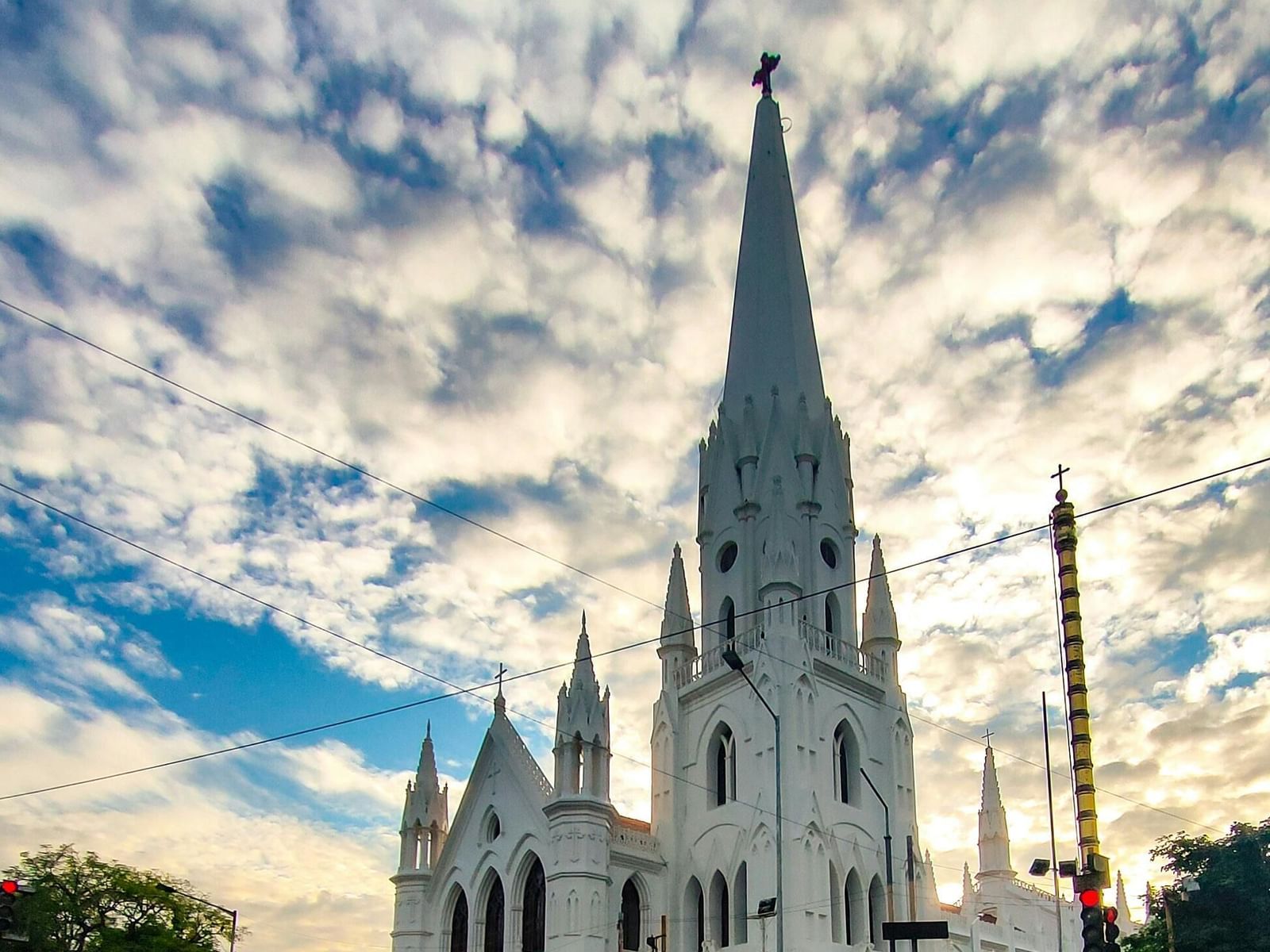 A white church with a tall steeple and intricate architectural details under a cloudy sky.