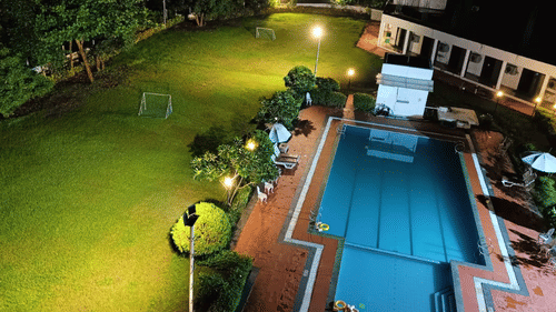 an aerial view of the lawn area next to the swimming pool as seen during the night with goal posts on the lawn and trees covering the surroundings. The lawn area is one of the best wedding venues in Silvassa at VITS Kamats Resort, Silvassa.