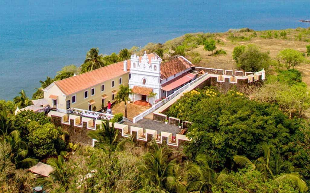 Aerial view of Fort Tiracol perched on a cliff's edge, overlooking a serene water body.