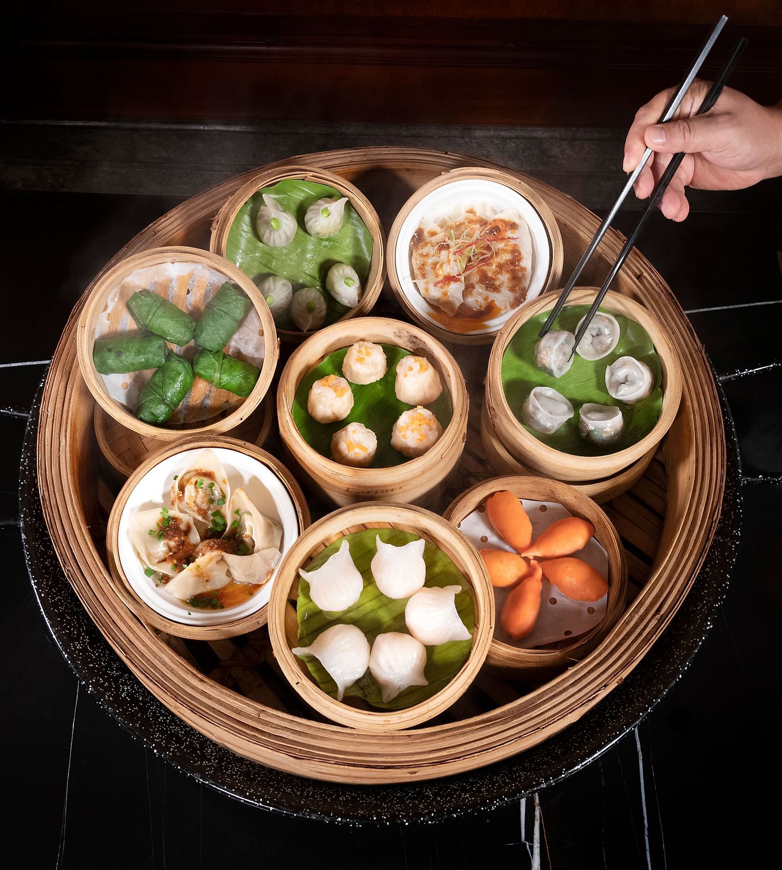 image of a well served steamed dishes that a person is trying to pick using a pair of chopsticks - The Claridges New Delhi