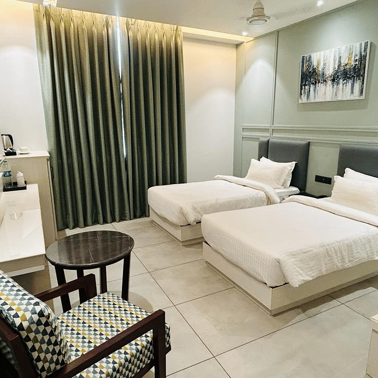 A room with twin beds, a sofa chair, coffee table, TV and a wall painting - Five Elements Hotels Goldleaf, Haldwani