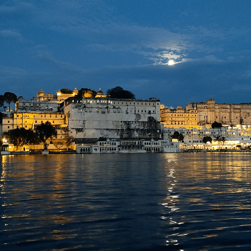 Illuminated City Palace and surrounding buildings reflecting across Lake Pichola at night