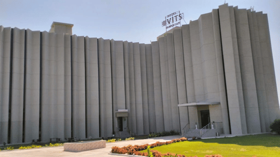 The facade of VITS Hotel in Jamnagar, Mithoi, on a sunny day featuring a multi-storey building surrounded by lawn under a clear sky.