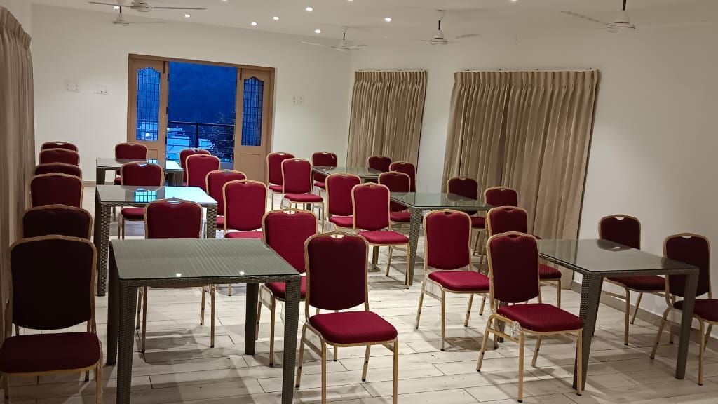 Close-up view of Green Park banquet hall with several red-coloured cushioned chairs arranged around several tables at WOW Naturefull Resorts.