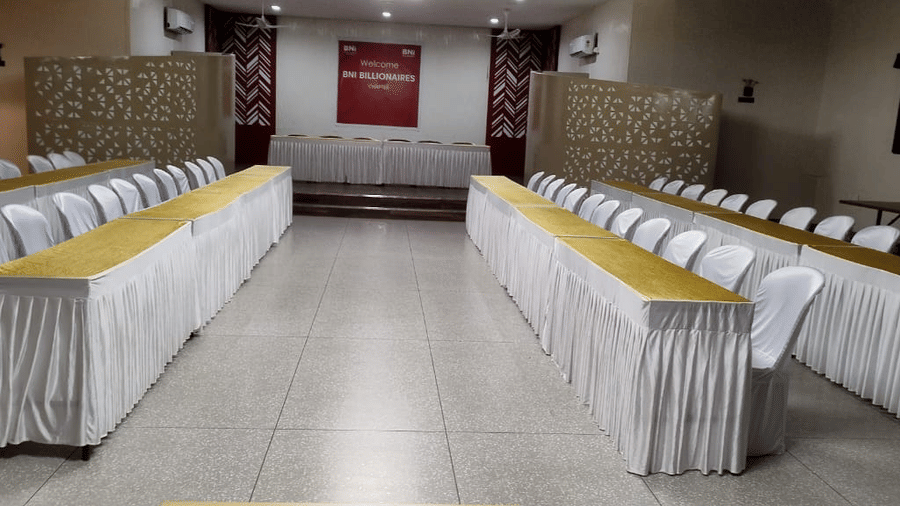 An event space with long tables covered in white cloths and lined with chairs - Lords Eco Inn Belagavi