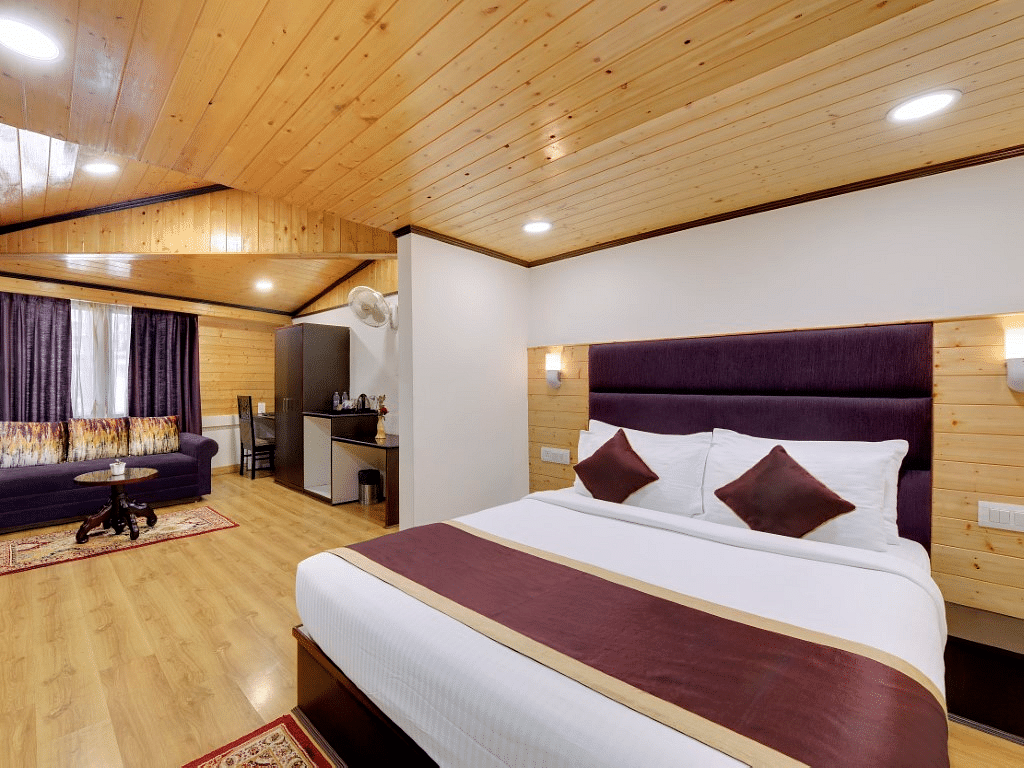 An image of a room with queen size bed leading to a living area with sofa, table and other amenities - Sumitel Darjeeling