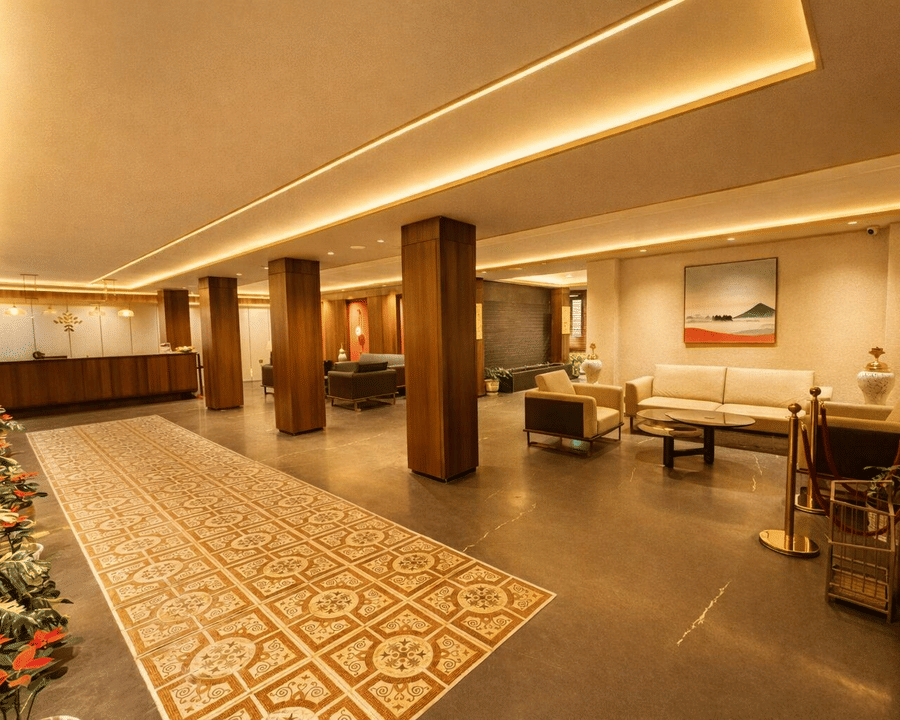 A lobby of Pride Premier Darjeeling featuring a reception desk, seating areas with sofa sets, a frame on the wall, and other decorative items.