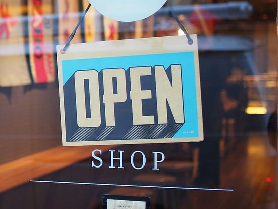 A sign board in hanging behind a close door with open written on it