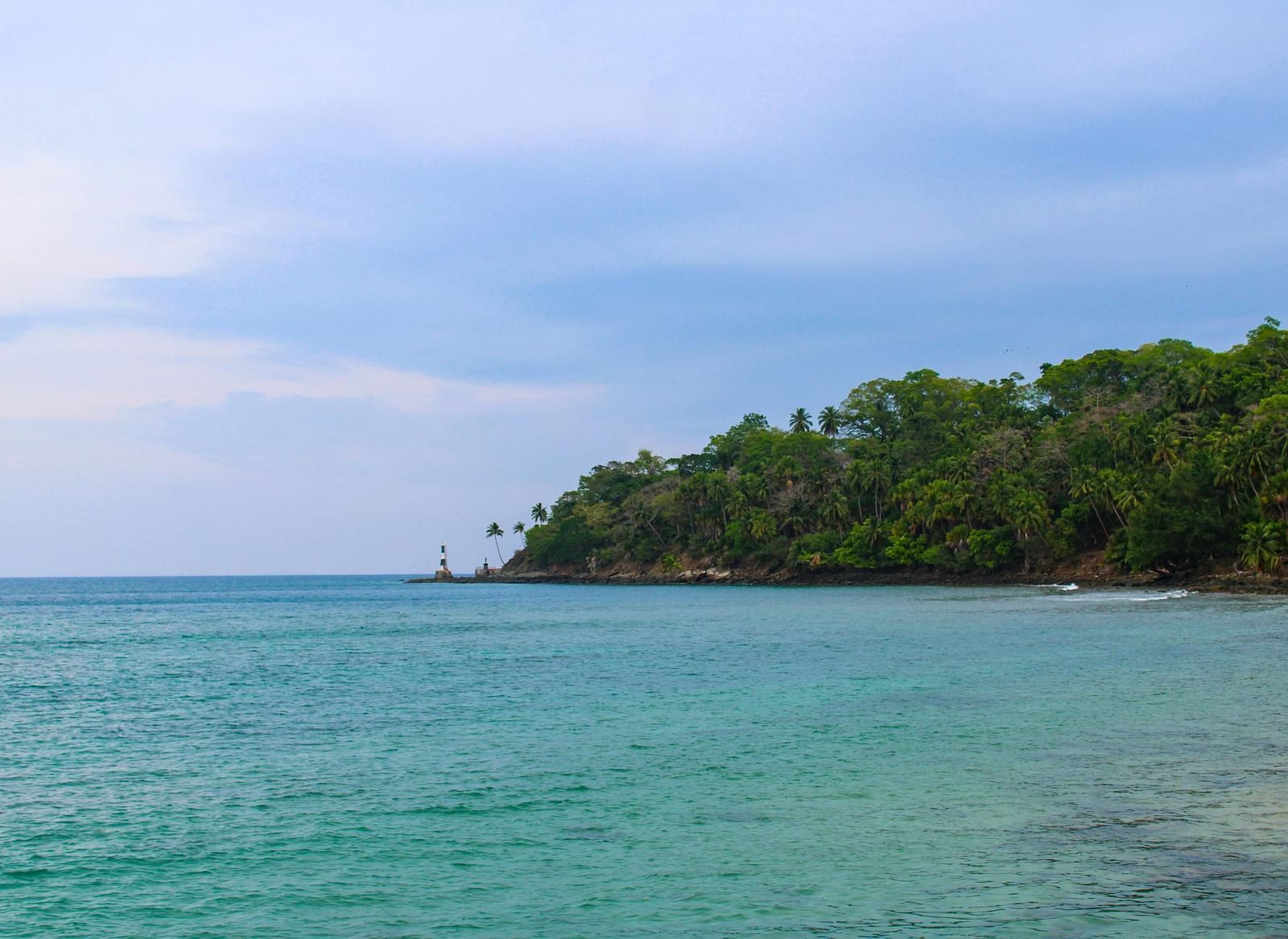Vast shoreline with gentle waves, surrounded by green trees and a serene blue sky.