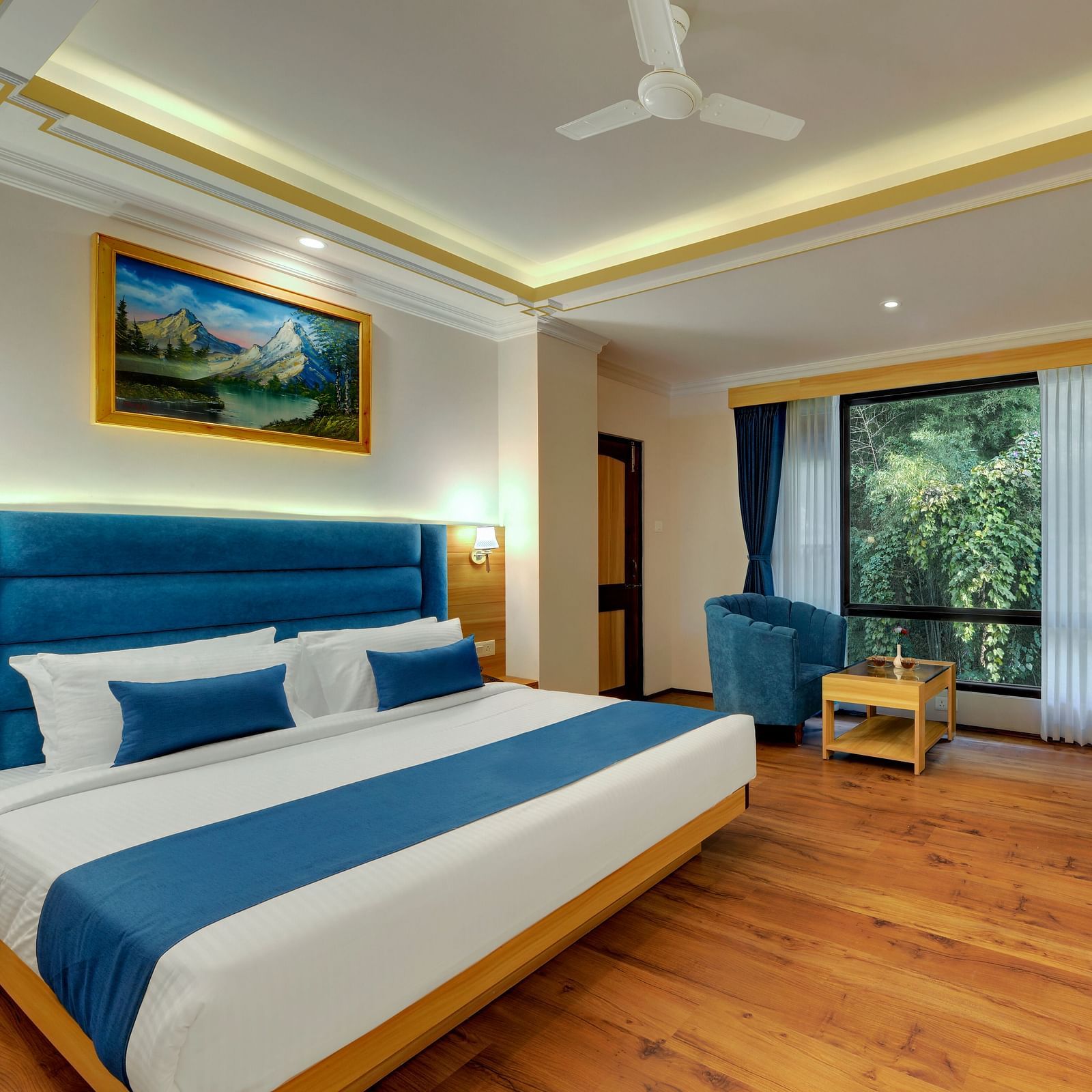 An image of a deluxe room with bed, sofa set, table, and an expansive window viewing the lush greenery - Yashshree Sikkim Blossom, Gangtok