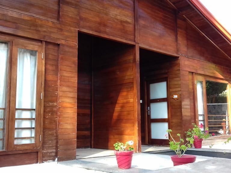 An image of a wooden cottage with expansive glass windows and flower pots placed near the entrance - GReaT trails Kodaikanal by GRT Hotels