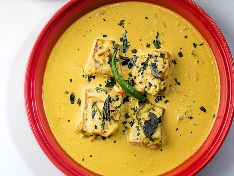 Plate of creamy yellow fish curry garnished with herbs and spices.