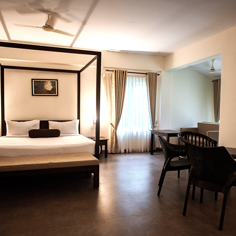 A spacious bedroom with a four-poster bed, elegant decor, and large windows at Abad Brookside Lakkidi, Wayanad.