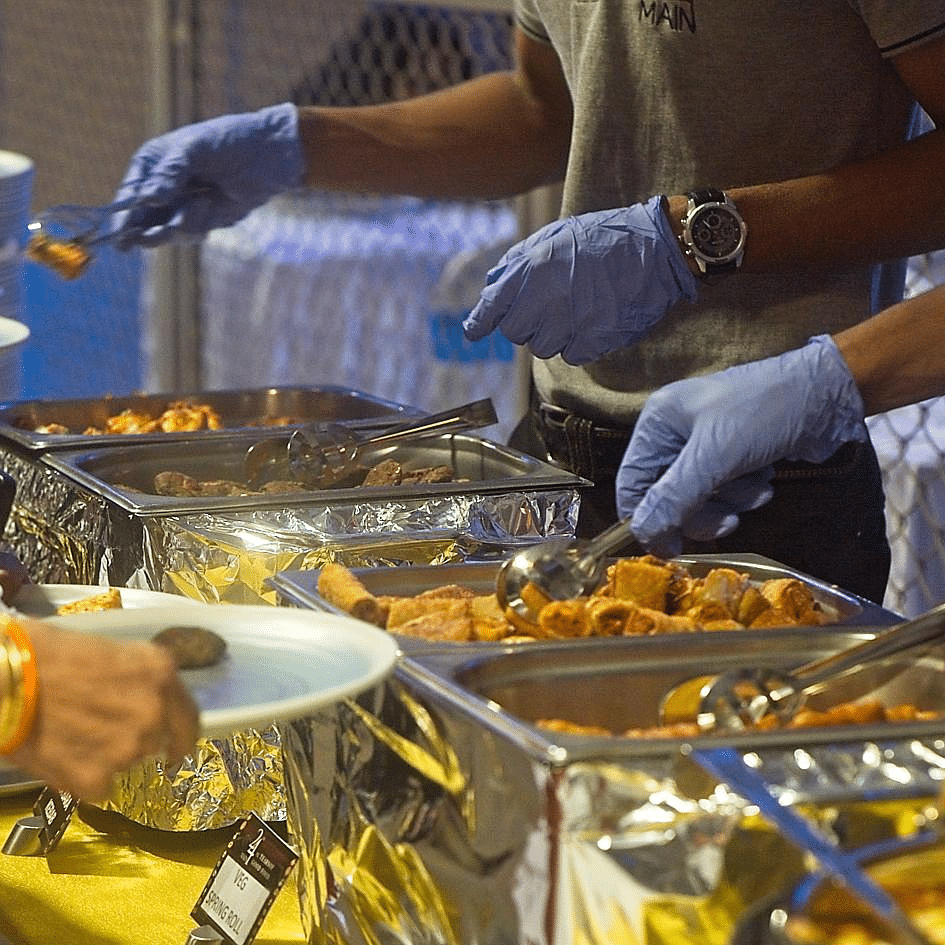 People serving food from chafing dishes onto plates at a buffet table.
