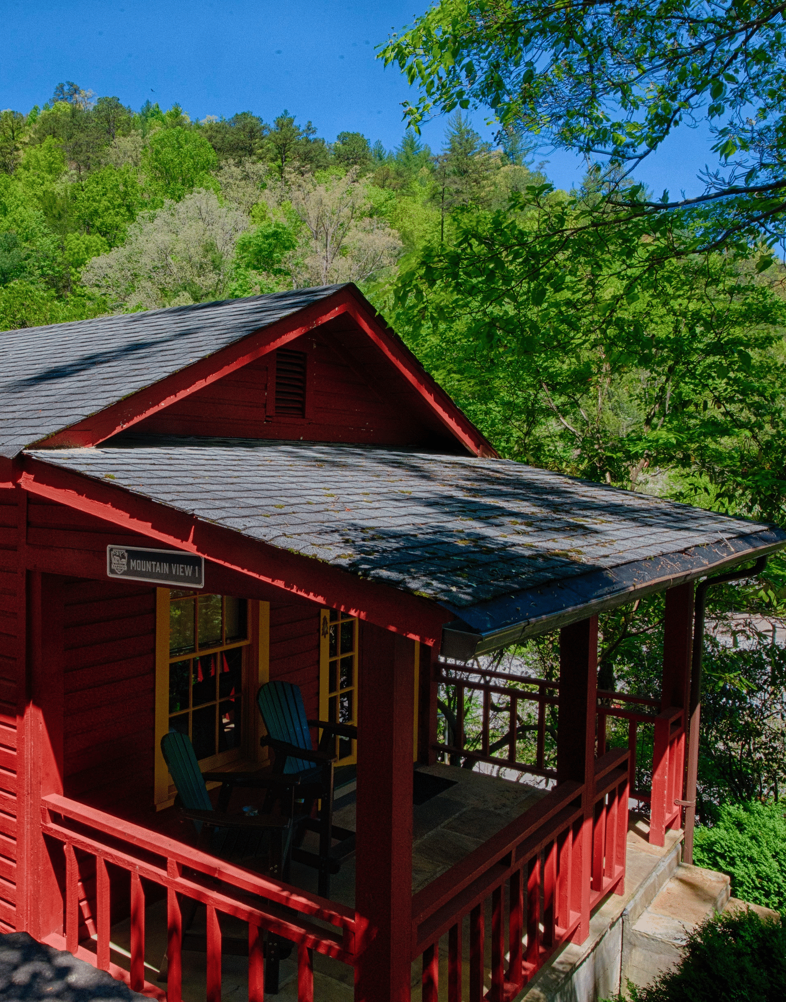 a bright facade image of a cabin win bright red colored exterior with lush green mountains in the background - Historic Tapoco Lodge