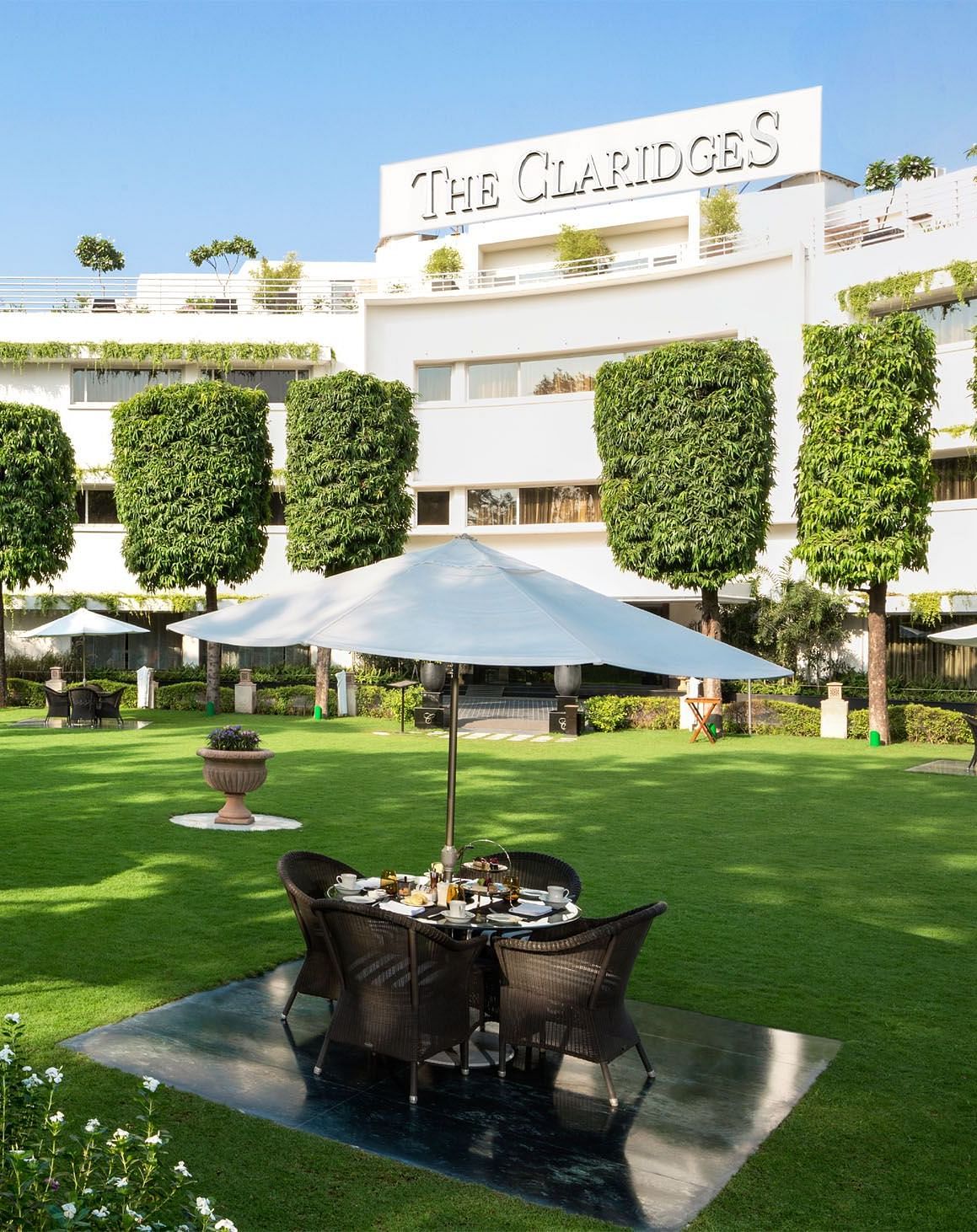 Facade of The Claridges New Delhi, featuring a green garden in the front and surrounded by towering trees, offering a serene and elegant ambience