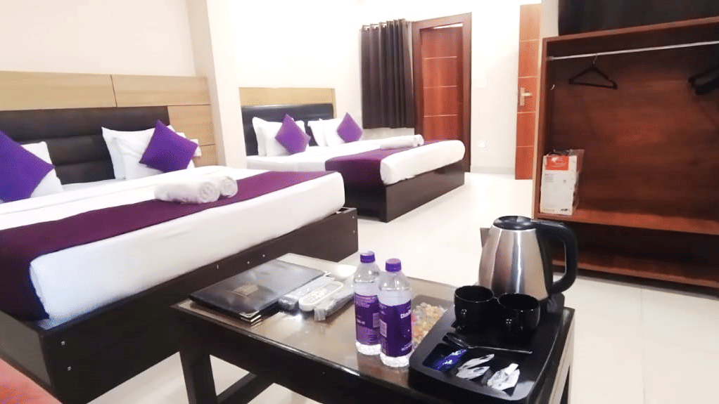 Interior view of a hotel room setup with multiple beds and a table at Perfectstayz Value Dwarkesh, Haridwar.