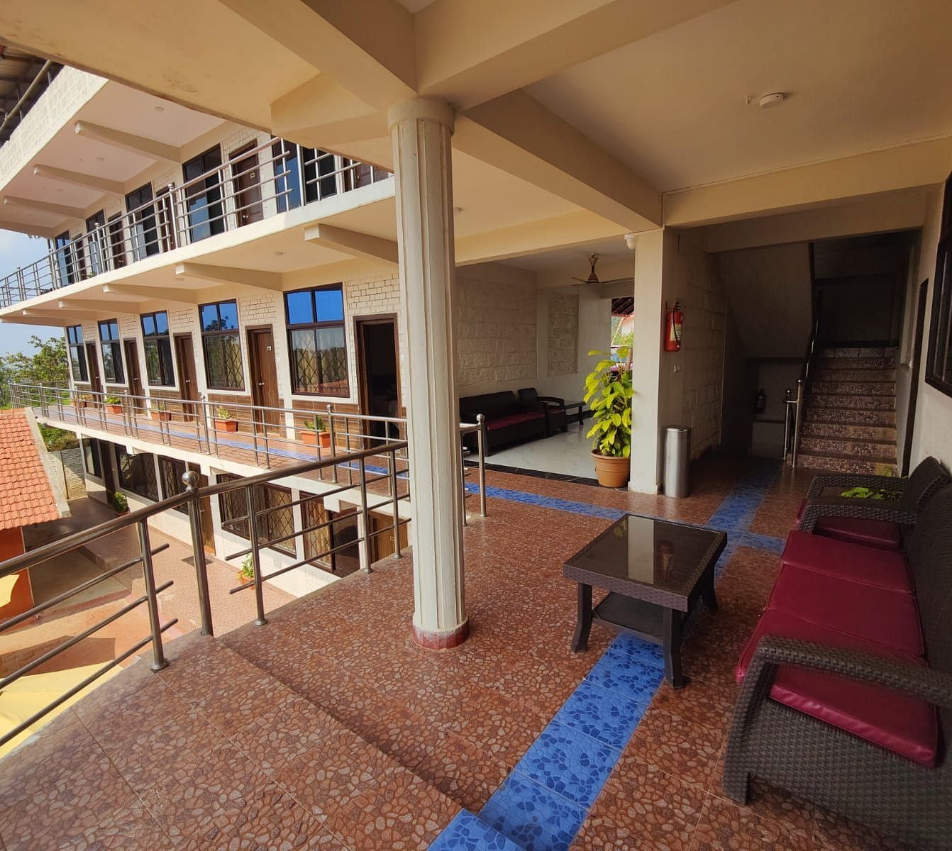 Tiled balcony with sofa and potted plants that overlooks a house, patio and greenery | Standard Room| Woodstock Resorts, Coorg
