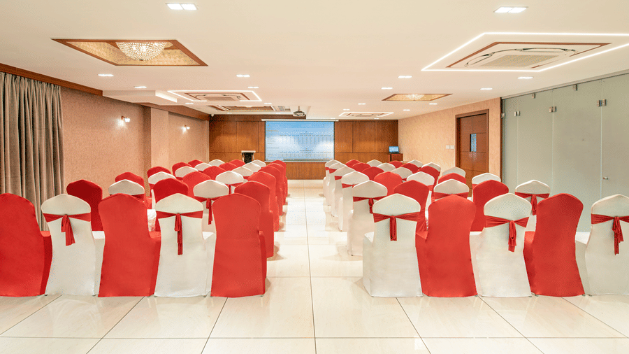 A banquet hall prepared for an event with long tables and chairs adorned with red sashes - SK Lords Inn Ahmedabad