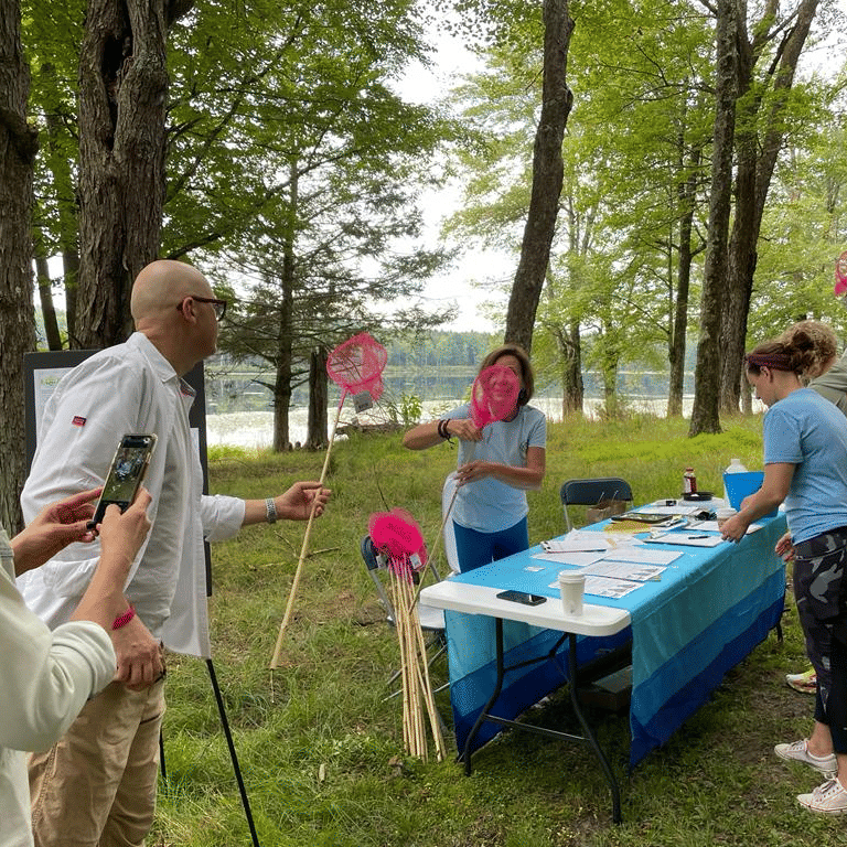 A group of people outdoors holding pink butterfly nets, gathered around a table with a person talking at YO1 Longevity & Health Resorts, Catskills