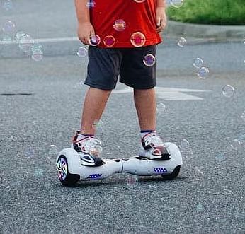 A toddler wearing a red t-shirt standing on a hoverboard with bubbles in front.