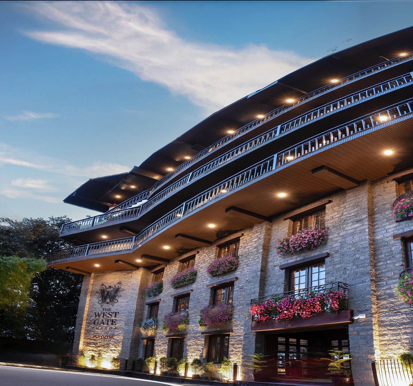 Front view of The West Gate Posada By Summit, Darjeeling, illuminated with lights and surrounded by lush greenery