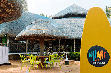 Outdoor cafe with thatched roof huts and vibrant seating near the entrance of a venue.