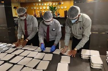 Hotel staff wearing masks and assembling meal boxes in a kitchen at a GRT Hotel.