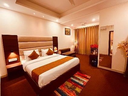 A spacious room with a bed, bed side tables, lamps, and a full length mirror - Five Elements Hotels, Haridwar