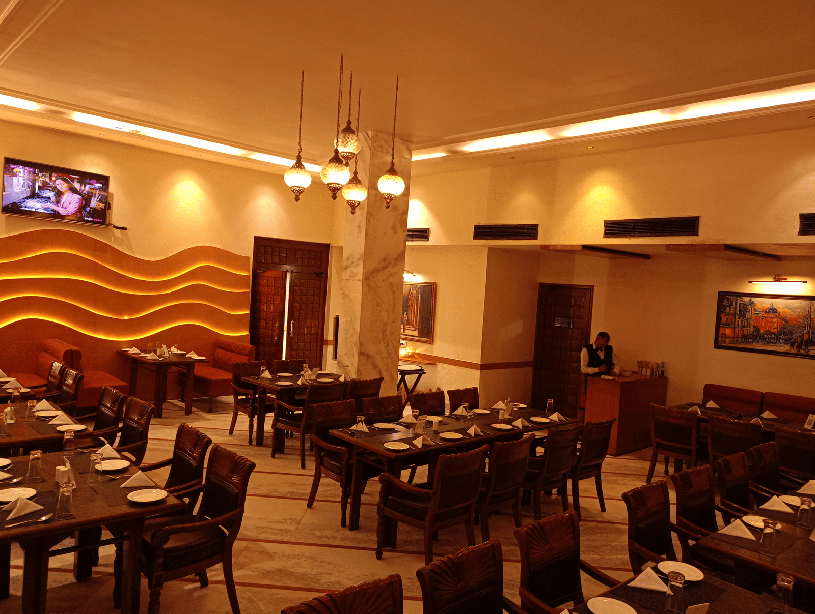 Dining area at Hotel Gold, Panipat featuring set tables, chairs, and a wavy patterned wall design.