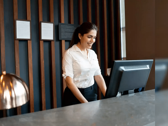 Image of a lady at a front desk with a computer in front of her.
