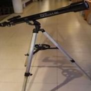 A black telescope is mounted on a tripod indoors