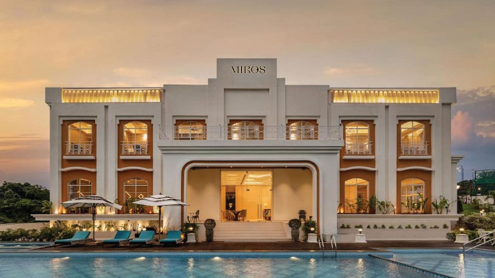 Full view facade of Miros Hotels with a calm swimming pool in the foreground along with beautiful sunset skies in the background.
