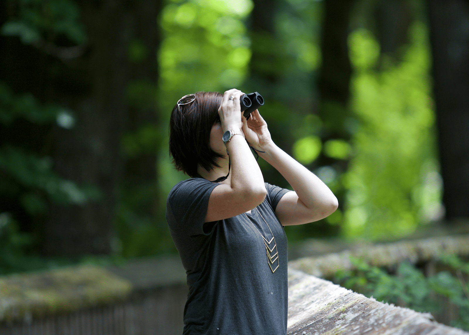 A woman looking through a pair of binoculars with a focused expression.