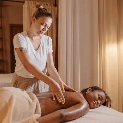 A therapist giving a back massage to a relaxed guest lying on a massage table in a softly lit room