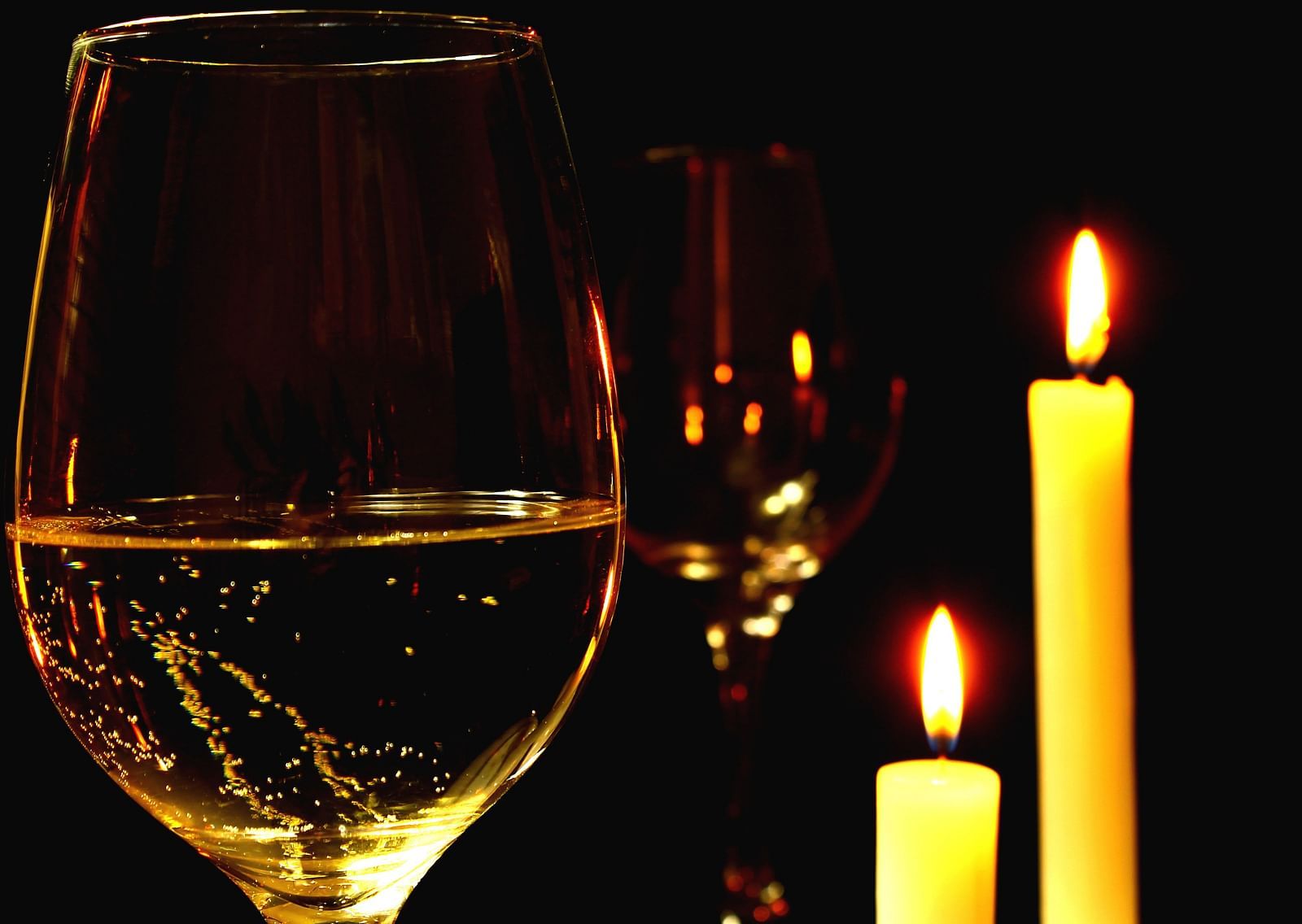 A close up shot of a wine glass with two lit candles next to the glass.